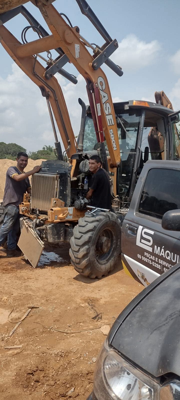 dois mecânicos consertando um radiador de uma retroescavadeira CASE 580N na terra, com um veículo da LS Máquin